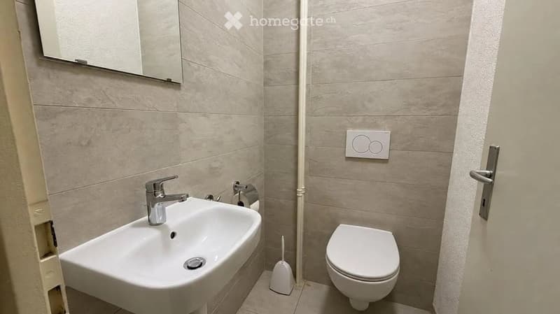 Modern bathroom with a white sink, chrome faucet, toilet, and a mirror above the sink. Beige tiled walls and floor.