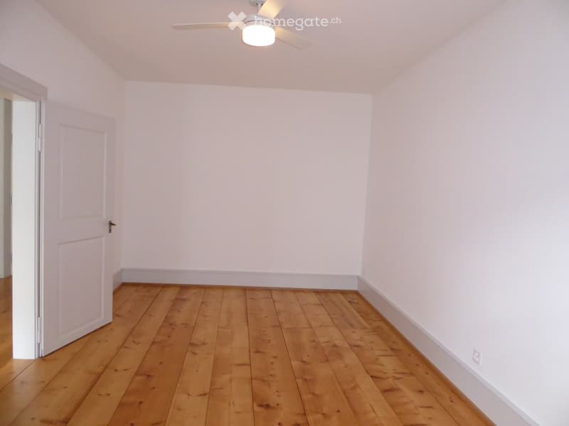 Empty room with wooden flooring, white walls, and a ceiling fan with light fixture. No furniture or equipment present.
