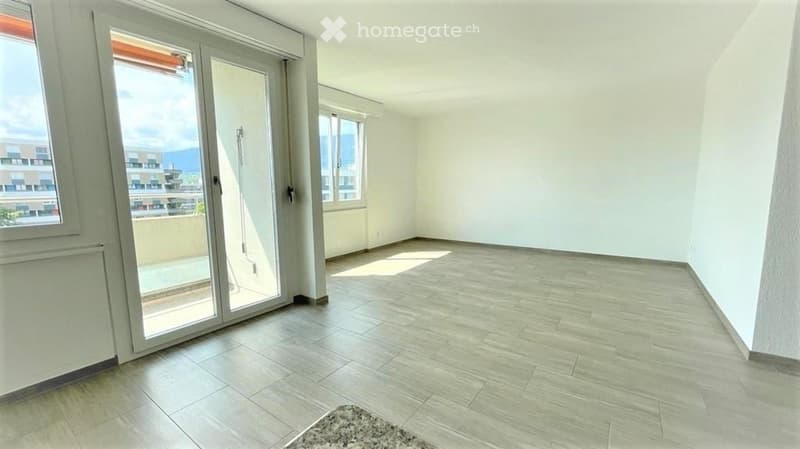 Empty room with light-colored tiled flooring, white walls, and large sliding glass doors leading to a balcony.