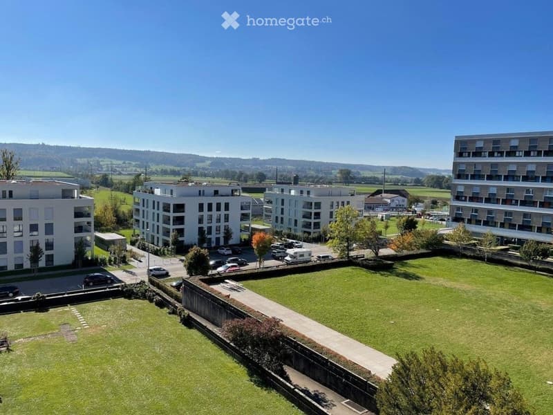 Aerial view of a modern residential complex with multiple buildings, parking area, and green spaces.