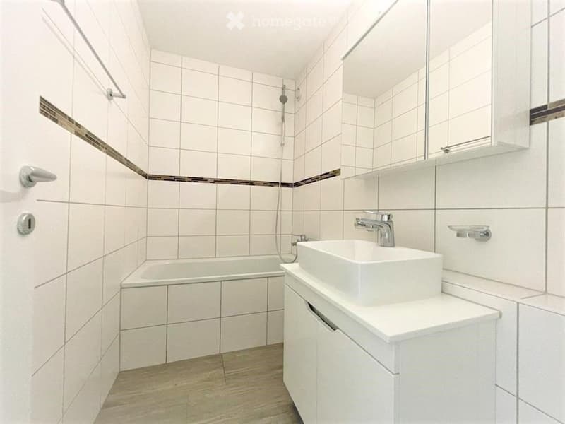 Modern bathroom with white tiles, a bathtub, a sink with a modern faucet, and a large mirror above the sink.