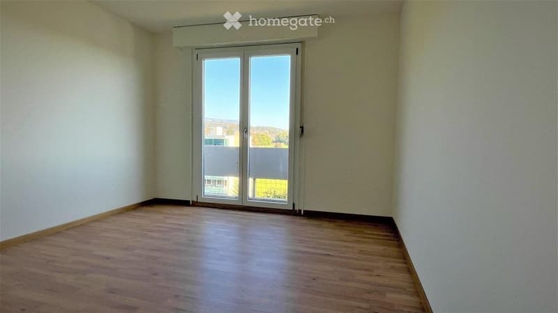 Empty room with wooden flooring, white walls, and large sliding glass doors leading to a balcony or outdoor area.
