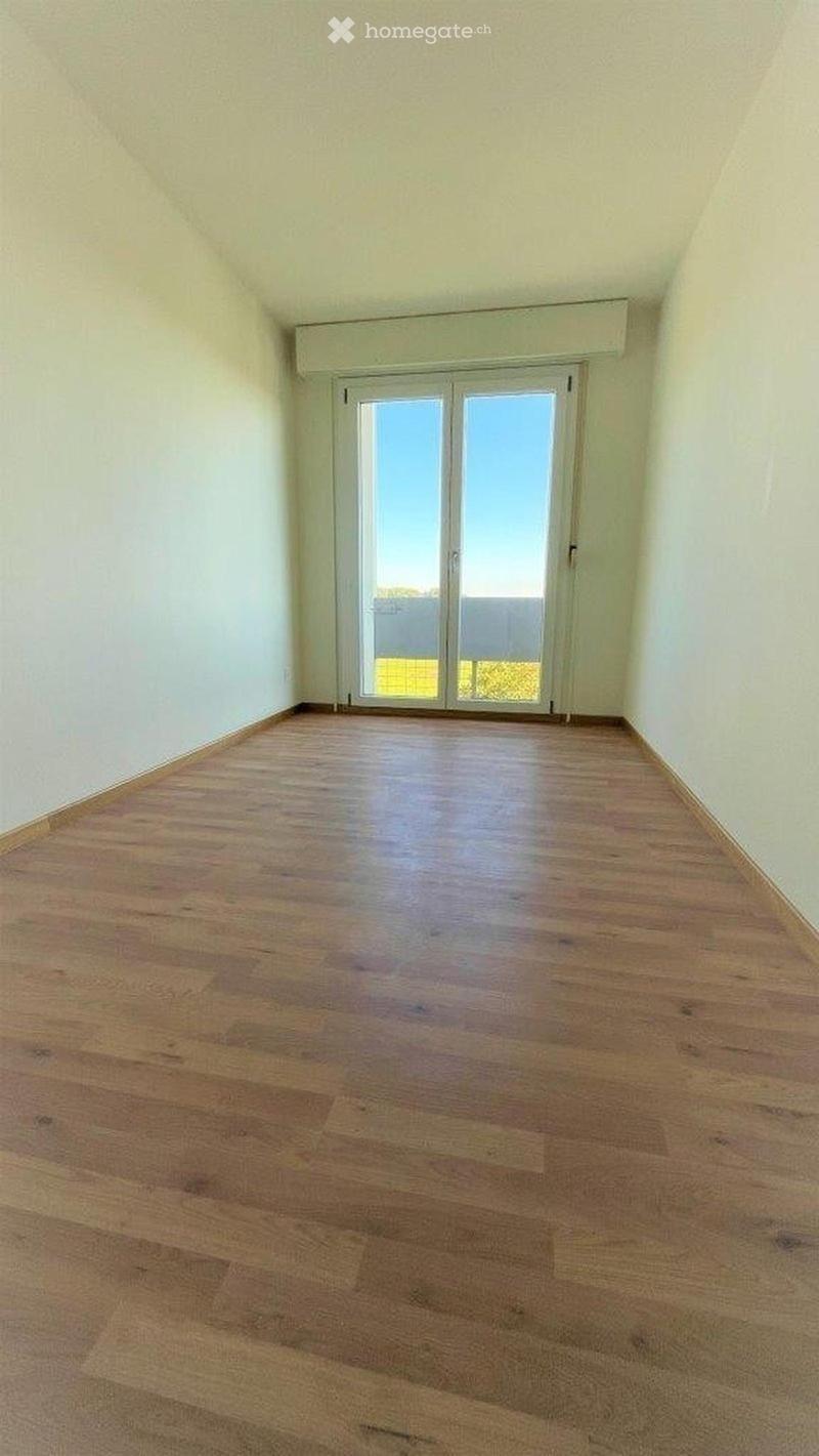 Empty room with wooden flooring and a large sliding glass door leading outside.