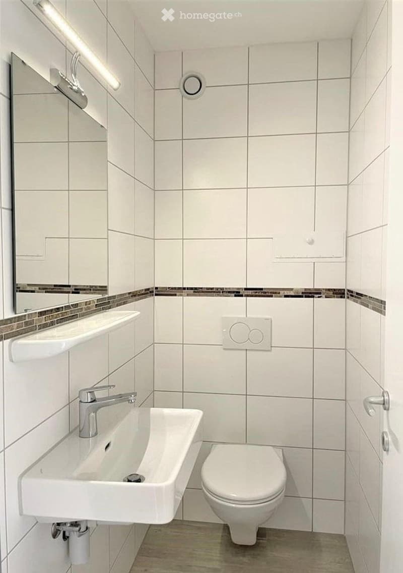Modern bathroom with white tiles, a sink with a chrome faucet, a toilet, and a mirror with a decorative border.