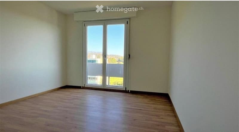 Empty room with wooden flooring, white walls, and large sliding glass doors leading to an outdoor area.