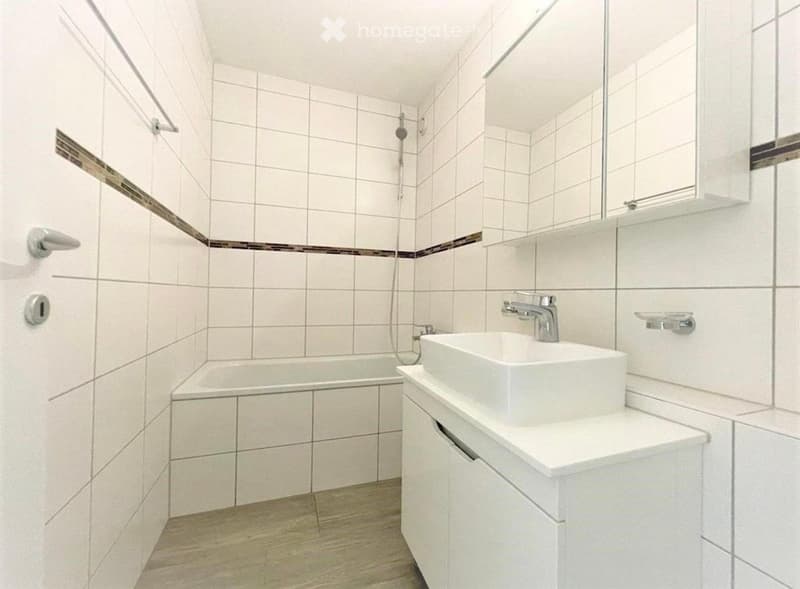 Modern bathroom with white tiled walls, a bathtub, a sink with a modern faucet, a mirror, and a white cabinet.