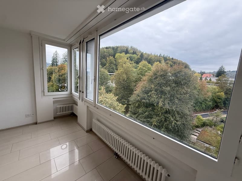 Empty room with tiled floor, large windows, radiators, and a view of trees and a house outside.