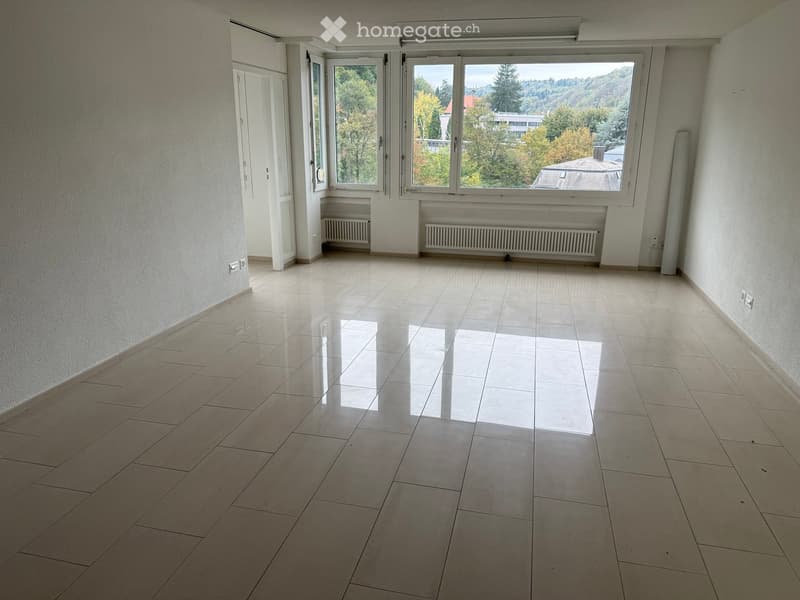 Empty room with tiled floor, large windows, radiators, and a door leading to another space.