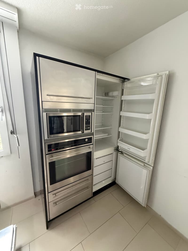 Modern kitchen with stainless steel appliances including a refrigerator, oven, and microwave. The refrigerator door is open, revealing empty shelves.