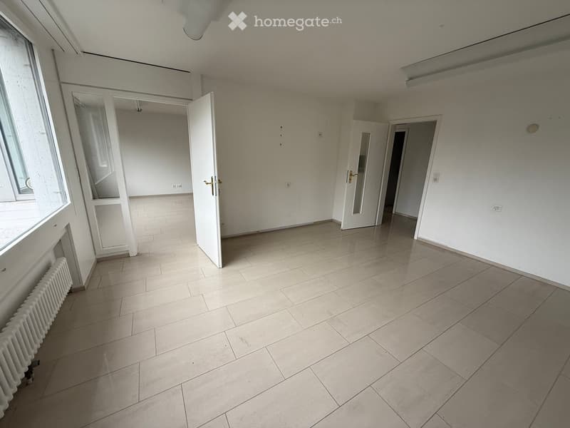 Empty room with tiled floor, white walls, and several doors leading to other spaces. A radiator is visible along the left wall.