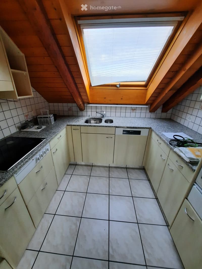 Modern kitchen with light-colored cabinets, granite countertops, and a tiled floor. Features a sink, dishwasher, and oven, with a skylight above.