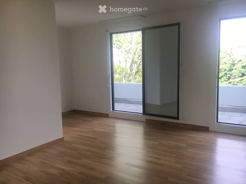 Empty room with wooden flooring, large sliding glass doors leading to a balcony, and white walls.