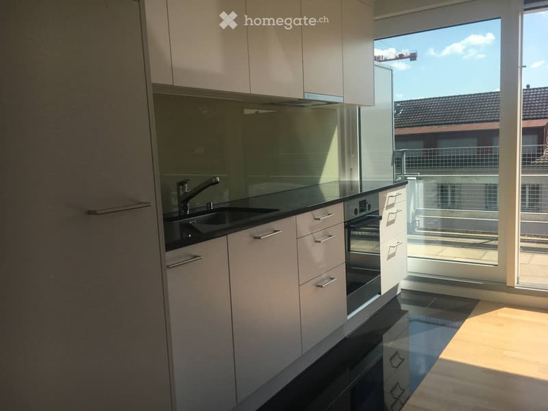 Modern kitchen with white cabinets, black countertops, a sink, and an oven. Large window offers a view of the balcony and surrounding area.