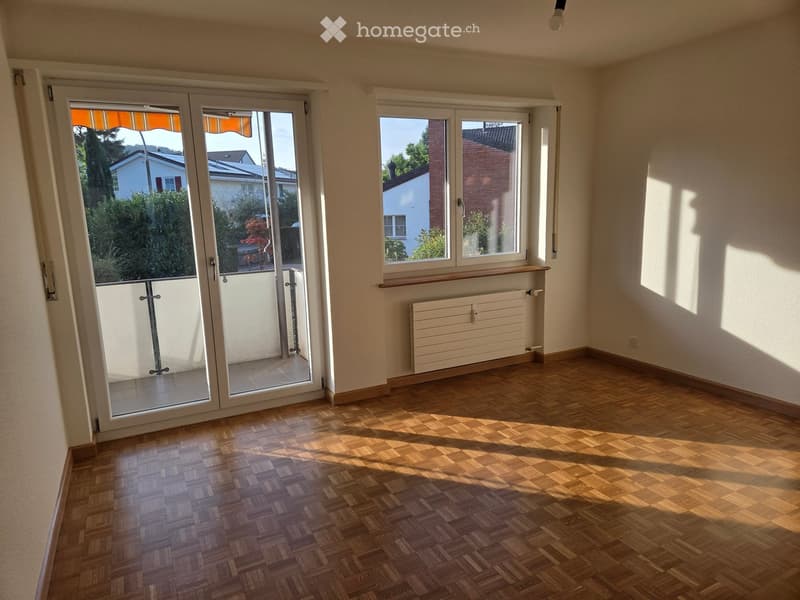 Empty room with wooden parquet flooring, large sliding glass doors leading to a balcony, and a radiator under a window.