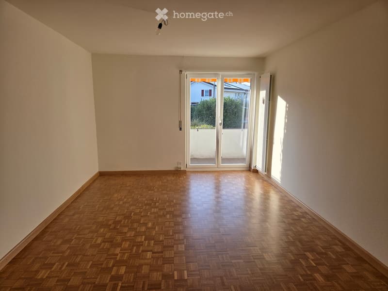 Empty room with wooden parquet flooring, white walls, and a large sliding glass door leading to a balcony.