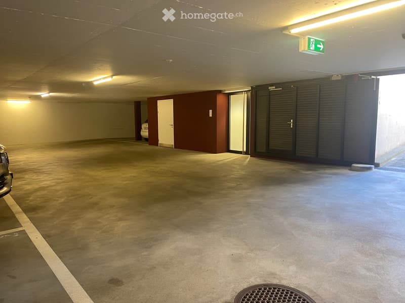 Underground parking area with concrete floors, fluorescent lighting, and a few parked cars visible in the background.