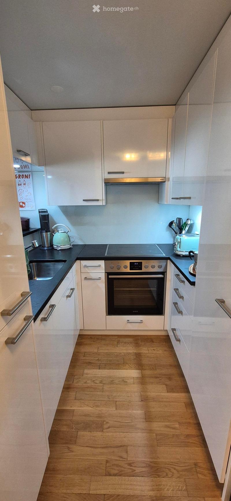 Modern kitchen with white cabinets, wooden flooring, and stainless steel appliances including an oven, induction stove, and coffee maker.