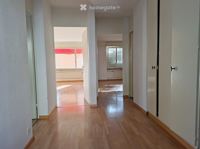 Empty hallway with wooden flooring, white walls, and doors leading to other rooms.