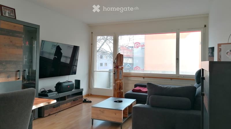 Modern living room with large windows, wooden floor, grey sofa, coffee table, TV, and speaker.