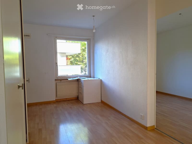 Empty room with wooden flooring, white walls, a window with blinds, a radiator, and a small cabinet.