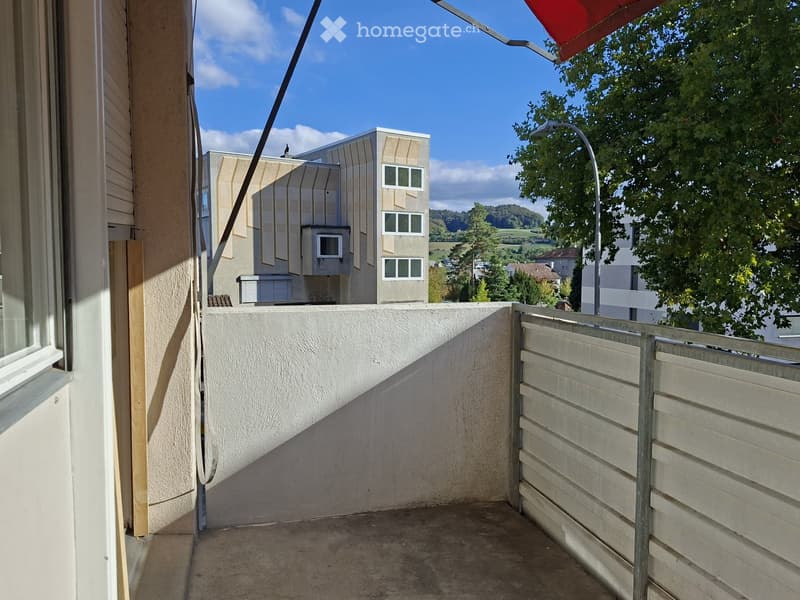 Balcony with a low concrete wall, wooden fence, and a view of a modern building and greenery.