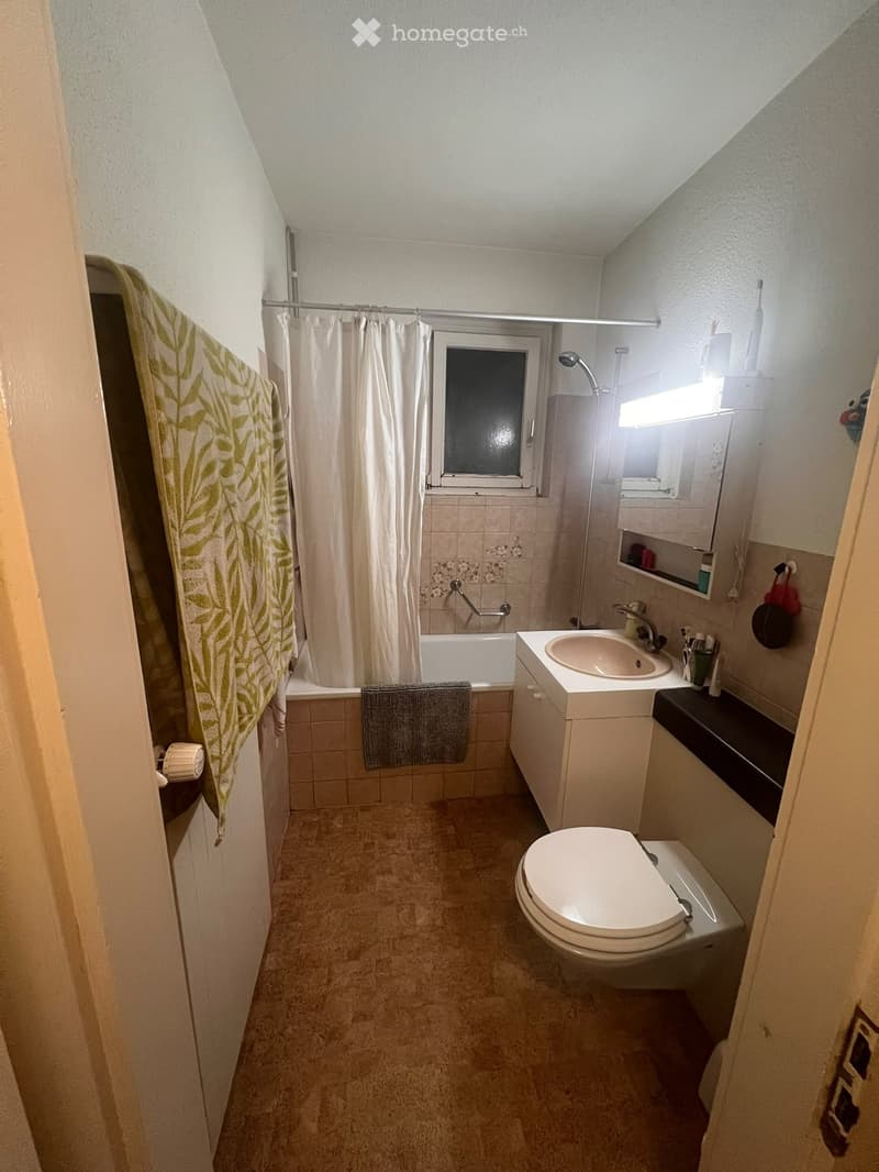 Compact bathroom with a bathtub, toilet, sink, and mirror. Features a shower curtain, towel, and a window providing natural light.