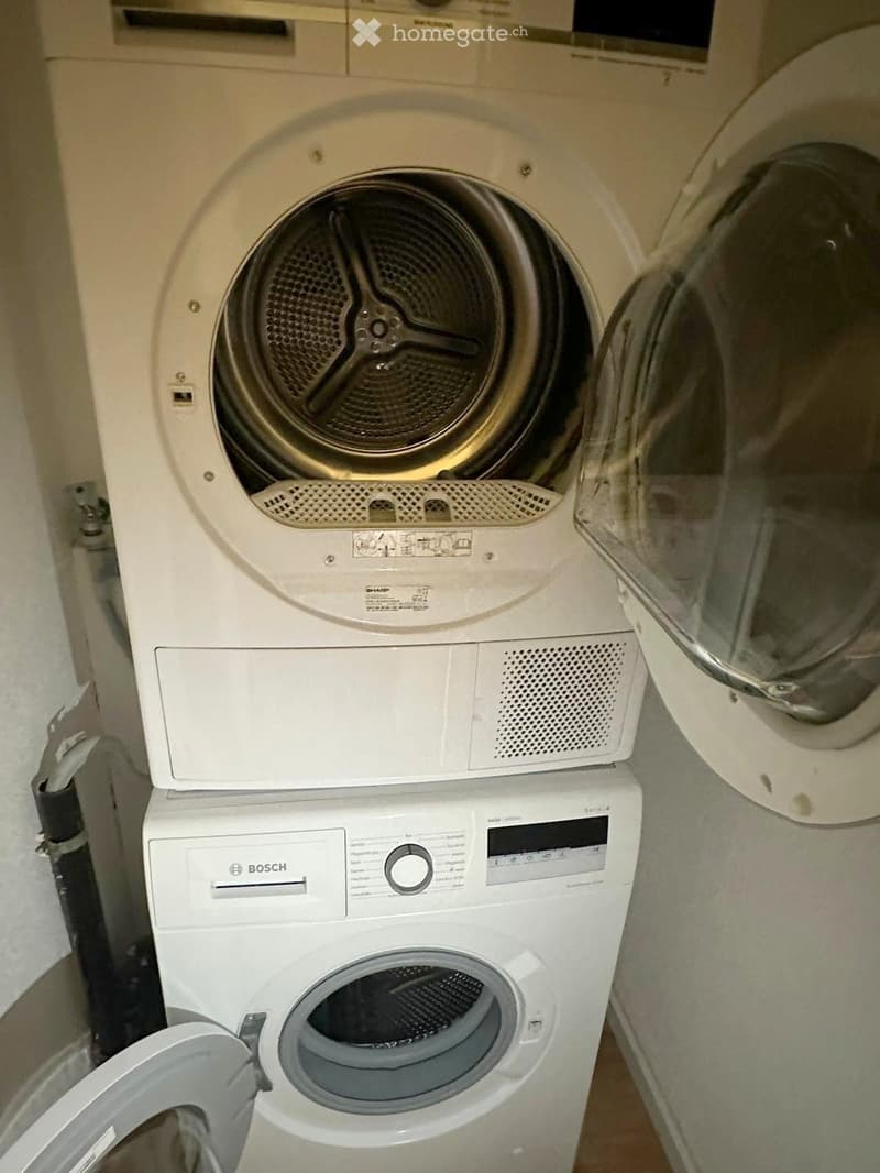 A compact bathroom with a Bosch washing machine and a Sharp dryer stacked vertically, both with open doors.