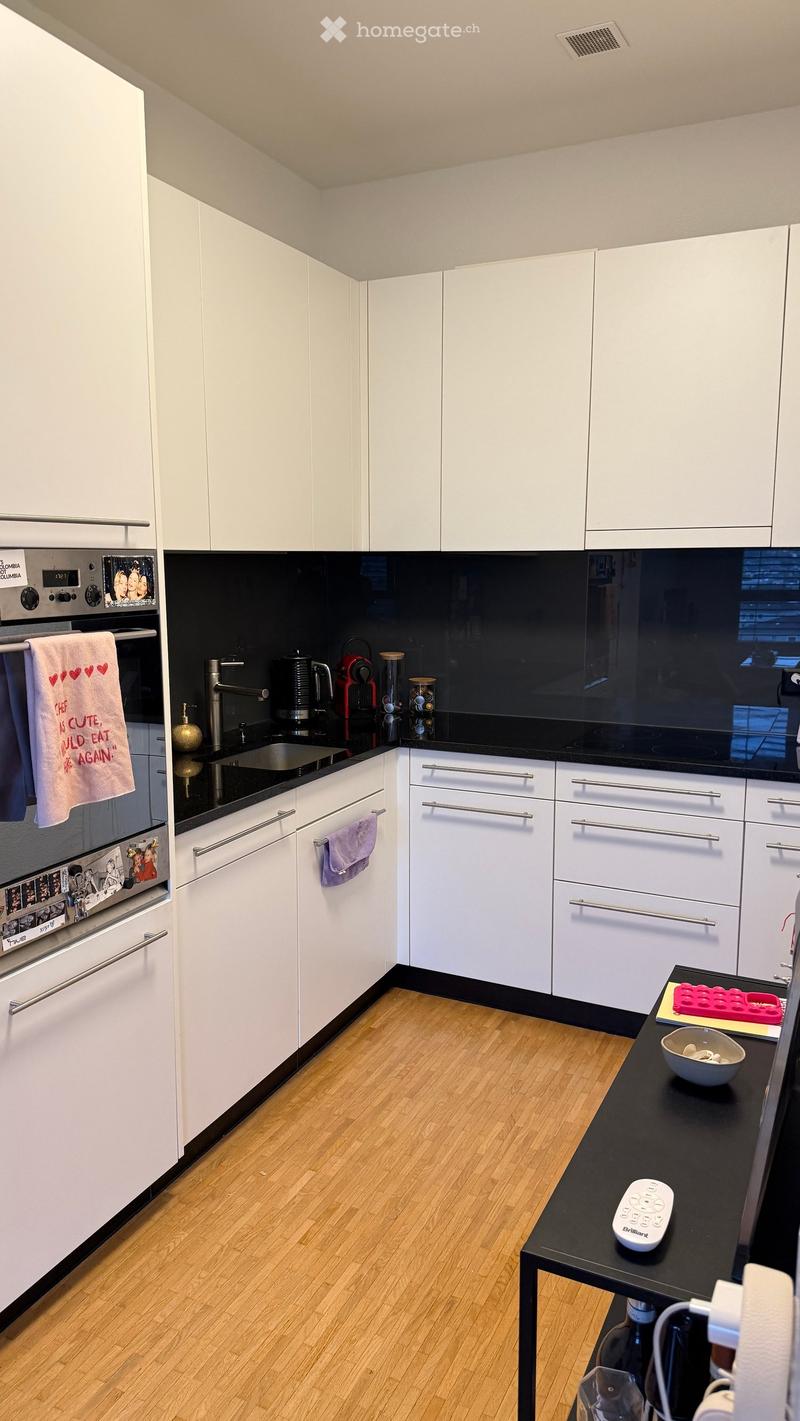 Modern kitchen with white cabinets, black countertops, stainless steel appliances, and wooden flooring.
