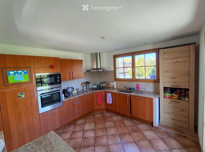 Modern kitchen with wooden cabinets, stainless steel appliances, and tiled flooring. Features an oven, microwave, sink, and various kitchen utensils.