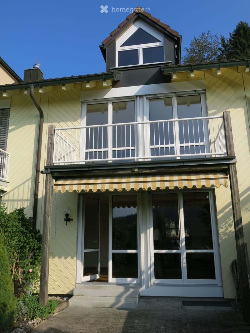 Two-story house with yellow siding, white trim, and a balcony with striped awning. Features large windows and a raised ground floor entrance.