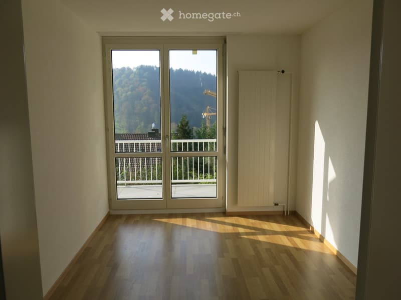 Empty room with wooden flooring, large glass doors leading to a balcony, and a radiator on the wall.