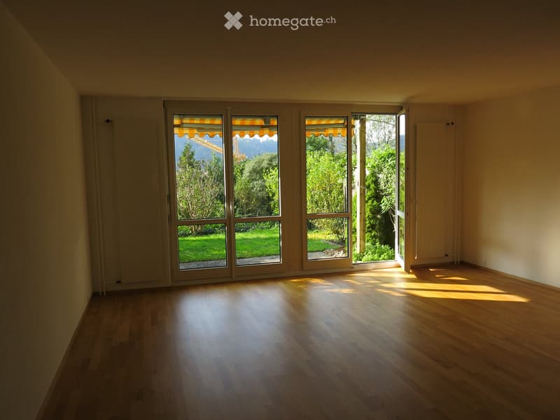 Empty room with wooden flooring and large sliding glass doors leading to a garden view.