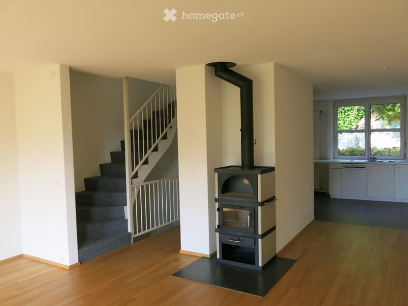 Hallway with wooden flooring, staircase leading upwards, and a wood-burning stove with chimney.
