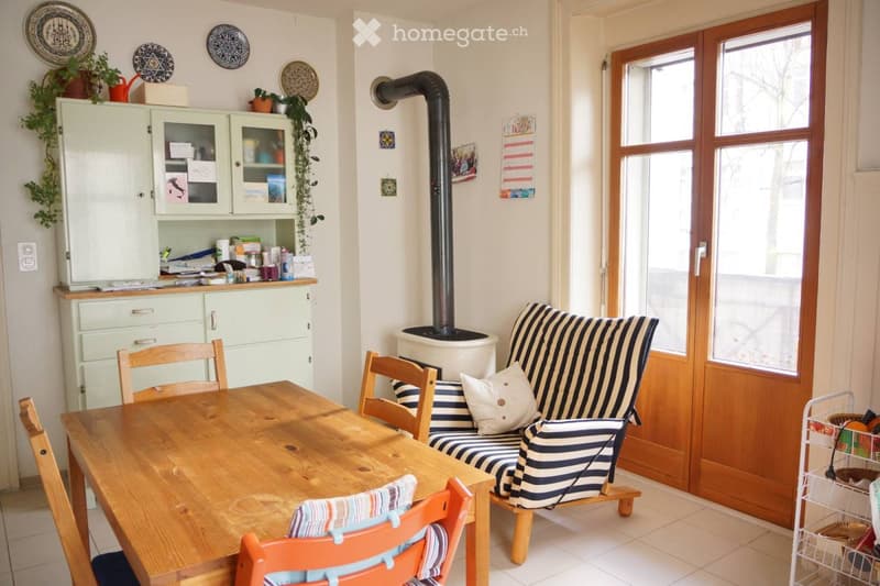 A cozy living and dining area with a wooden dining table, chairs, a striped sofa, a cabinet, and a fireplace.
