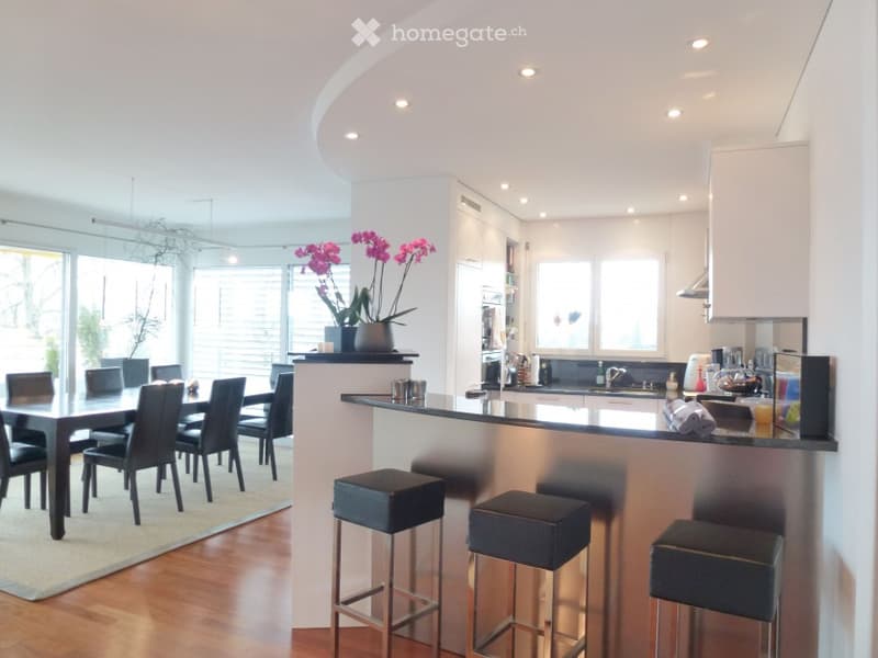 Modern open-plan kitchen and dining area with a sleek black dining table and chairs, a kitchen island with bar stools, and contemporary kitchen cabinets and appliances.