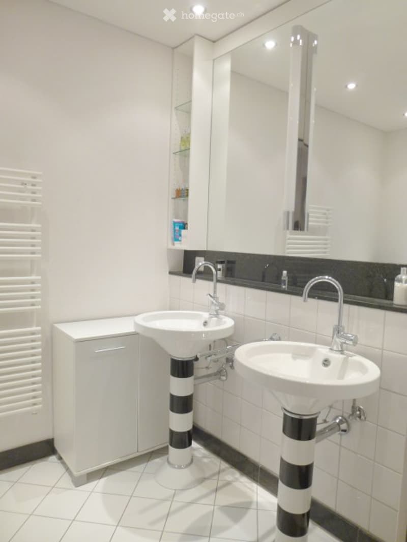 Modern bathroom with two white sinks, large mirror, white cabinet, and sleek chrome faucets.