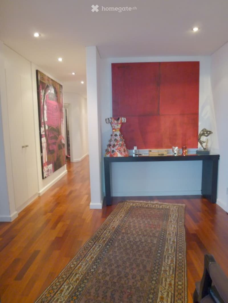 Elegant hallway with polished wooden flooring, recessed ceiling lights, a large red accent wall, and a decorative console table with a colorful sculpture and small items on top.