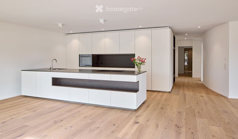 Modern kitchen with white cabinets, dark countertops, and a central island. Features include a sink, faucet, oven, and a vase with flowers on the island.