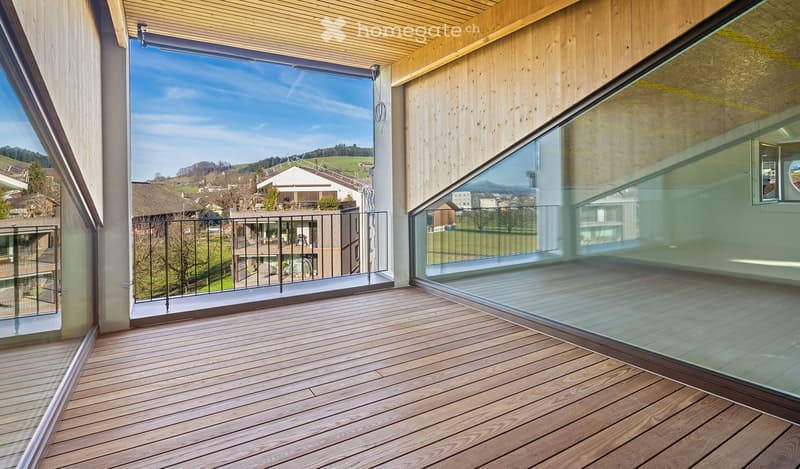 Modern wooden balcony with glass railings, overlooking a scenic countryside view.