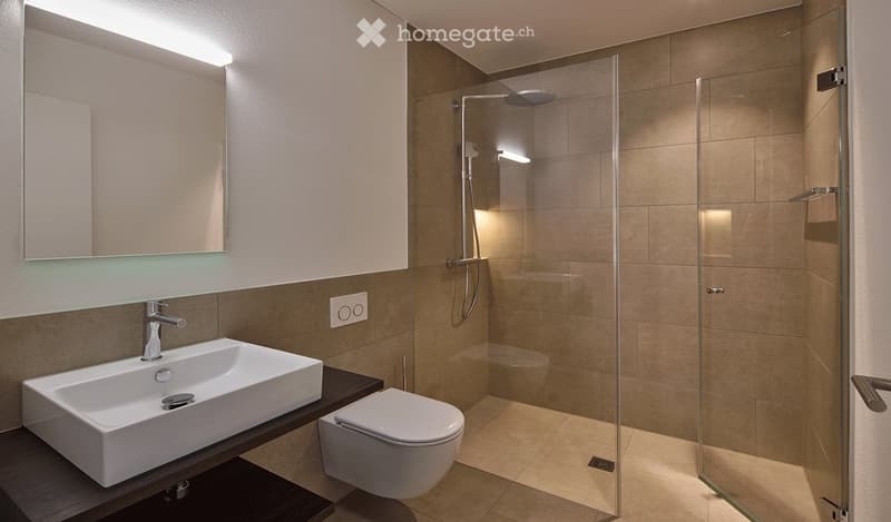 Modern bathroom with a white sink, toilet, glass-enclosed shower, and a large mirror with built-in lighting.
