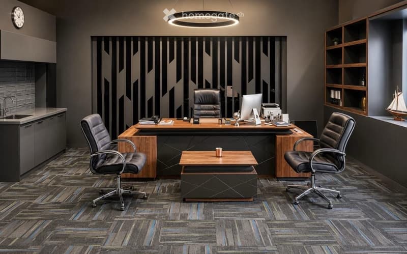 Modern office space with a large wooden desk, ergonomic chairs, a small coffee table, and a sleek round pendant light. Shelves hold books and decorative items, including a model ship.