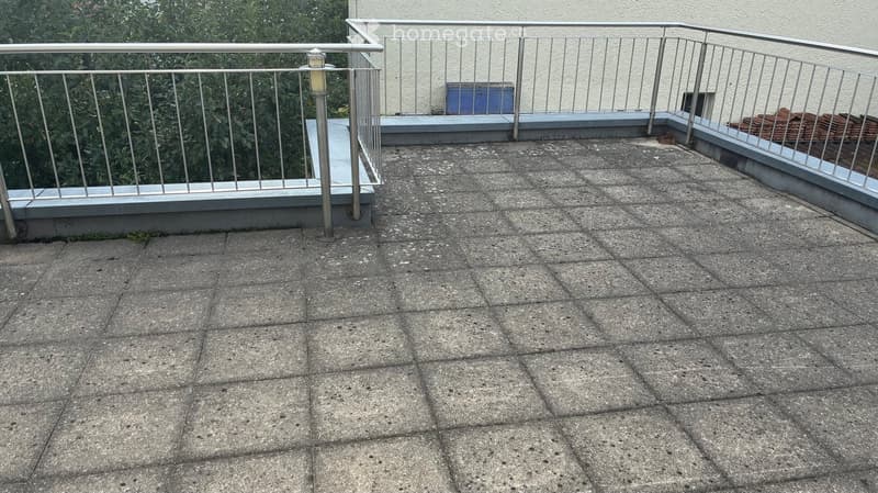 Empty rooftop terrace with concrete tiles, metal railing, and a small lamp post.