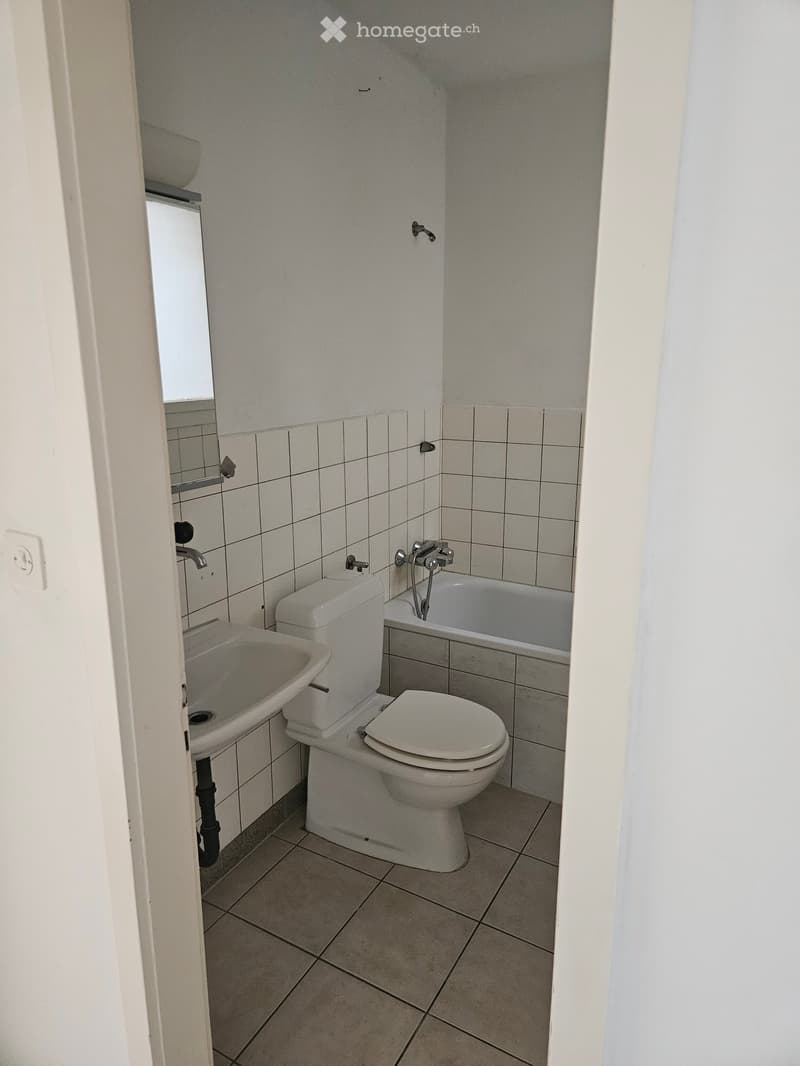 Small bathroom with white tiled walls, a toilet, a sink, and a bathtub.