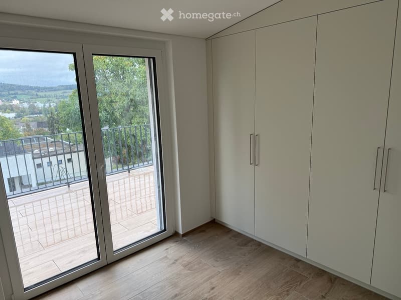 Empty room with wooden flooring, white built-in wardrobes, and a large sliding glass door leading to a balcony with a scenic view.