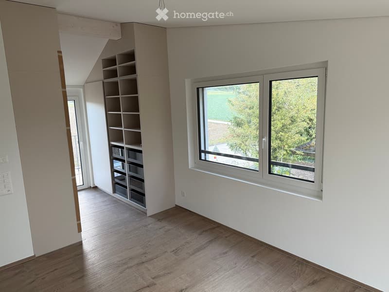 Empty room with wooden flooring, white walls, large windows, and built-in shelving unit.