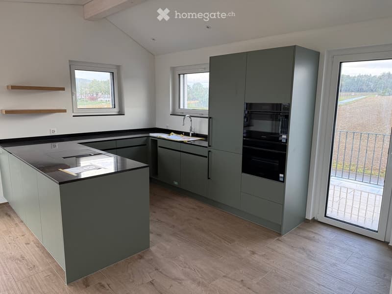 Modern kitchen with grey cabinets, a central island, and a large window overlooking a rural landscape.