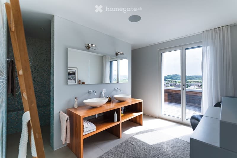 Modern bathroom with a wooden vanity, two sinks, a large mirror, and a view of the outdoors through a large window.