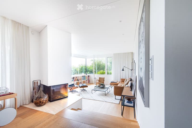 Bright living room with large windows, fireplace, sofa, coffee table, chairs, bookshelf, and floor lamp.
