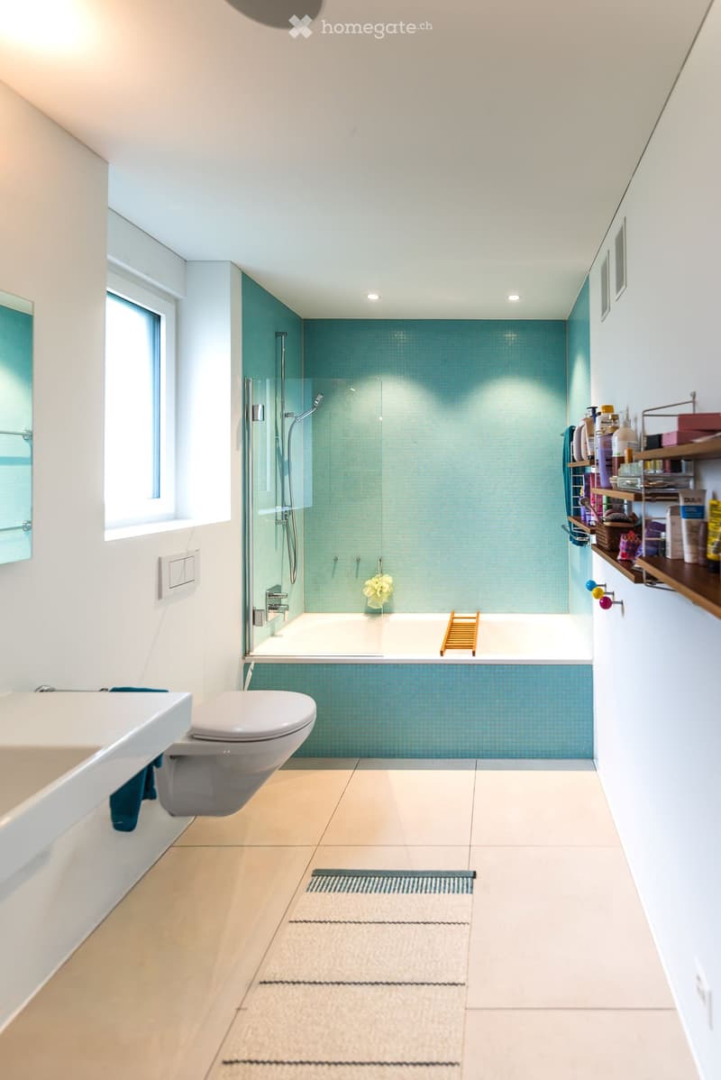 Modern bathroom with a bathtub, toilet, glass-enclosed shower, and wooden shelf with toiletries.