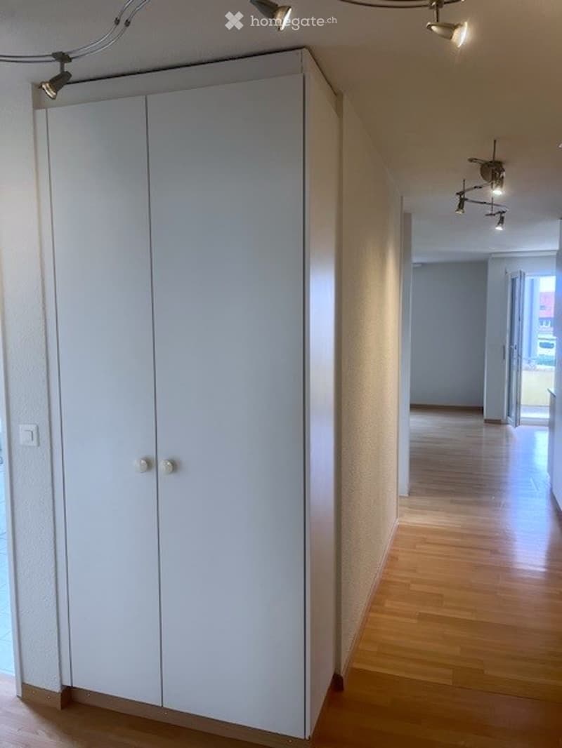 Empty hallway with wooden flooring, white walls, and a built-in white closet with double doors.